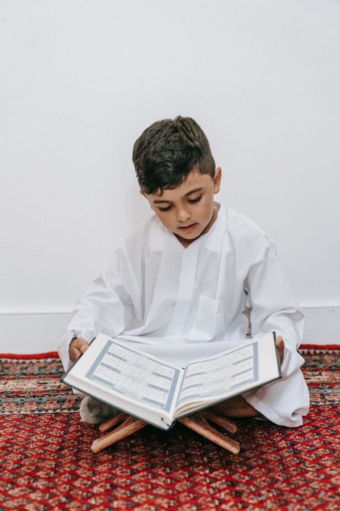 The Art of Drawing Readers In: Your attractive post title goes here A child sits cross-legged reading a holy book indoors, emphasizing cultural and religious learning.